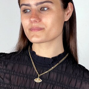 May include: A gold chain necklace with a small, eye-shaped pendant. The pendant is decorated with small, clear stones.