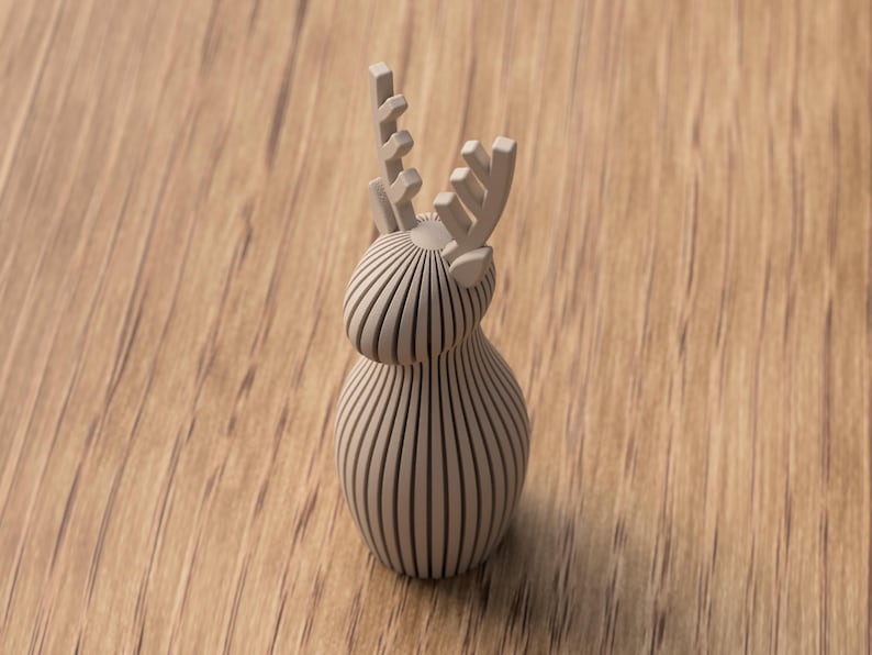 Puede incluir: Figura de reno de madera marr&oacute;n claro con un dise&ntilde;o de rayas verticales. El reno tiene un cuerpo redondeado y astas detalladas. La figura est&aacute; sobre un fondo de madera.