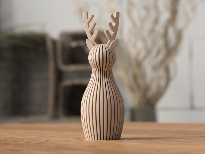 Puede incluir: Una figura de ciervo de madera de color marr&oacute;n claro. El ciervo tiene un cuerpo delgado con l&iacute;neas verticales y un par de cuernos. La figura est&aacute; sobre una superficie de madera.