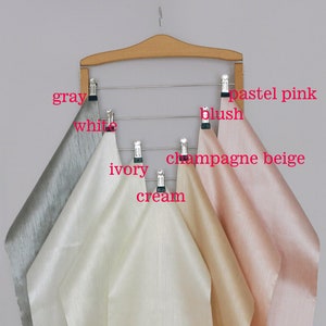 Six fabric swatches hanging on a wooden hanger. The swatches are in the colors gray, white, ivory, cream, champagne beige, and pastel pink.