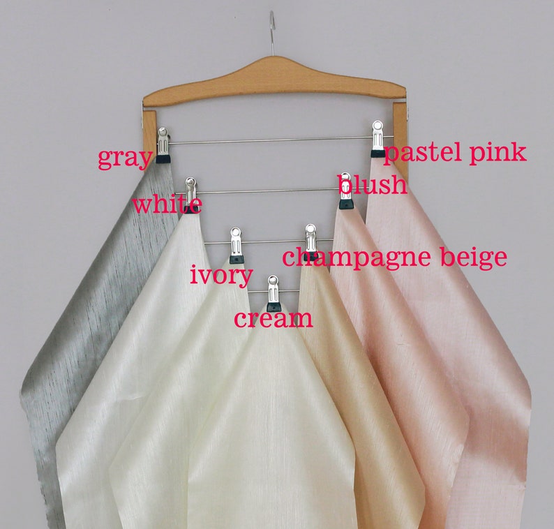 Six fabric swatches hanging on a wooden hanger. The swatches are in the colors gray, white, ivory, cream, champagne beige, and pastel pink.