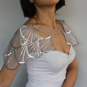 Front view of the silver bridal shoulder jewelry, with geometric sequin embroidery, wing-shaped shoulder panels and fine chain details framing the neckline.