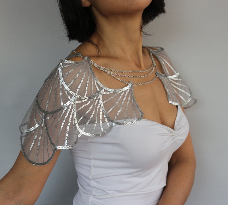 Front view of the silver bridal shoulder jewelry, with geometric sequin embroidery, wing-shaped shoulder panels and fine chain details framing the neckline.
