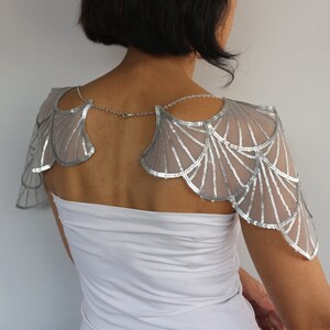 Back view of the silver sequin bridal shoulder capelet, showing the embroidered wing-shaped panels and delicate aluminum chains draped across the upper back.