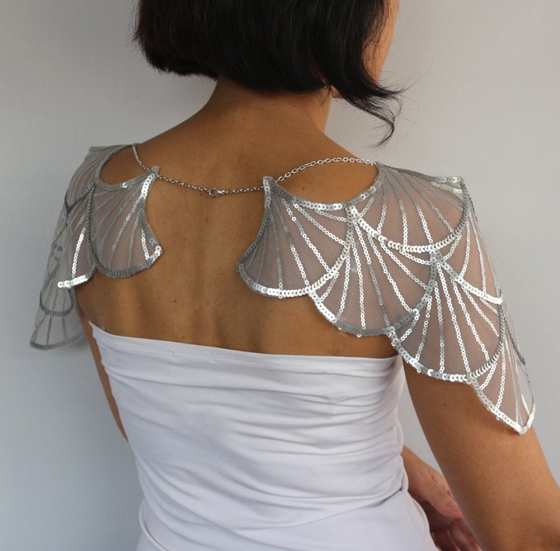 Back view of the silver sequin bridal shoulder capelet, showing the embroidered wing-shaped panels and delicate aluminum chains draped across the upper back.
