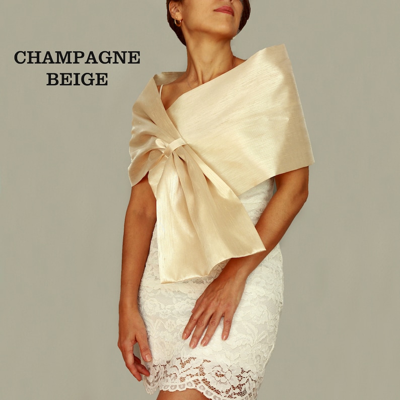 A champagne beige satin shawl with a bow tied at the front. The shawl is draped over a white lace dress.