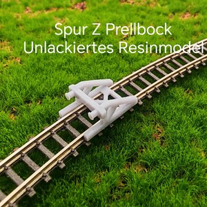 Può includere: Un respingente per treni modello grigio, posizionato su una sezione di binari ferroviari in miniatura. I binari sono posizionati su uno sfondo di erba artificiale verde. Il testo "Spur Z Prellbock Unlackiertes Resinmodel" è visibile.