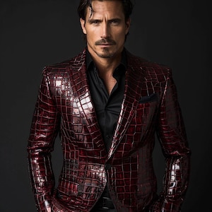 Puede incluir: Un blazer burdeos con un patrón de piel de cocodrilo. Se lleva sobre una camisa negra. El hombre de la foto tiene el pelo oscuro y un bigote.