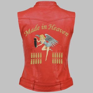 May include: Red leather vest with the words "Made in Heaven" in gold script. The back features a pin-up angel graphic holding a bomb, with rows of gold bomb graphics below. The vest has a fitted silhouette and a belt.