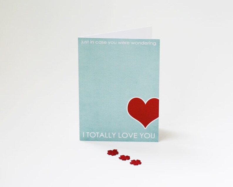 May include: A light blue card with the text "Just in case you were wondering, I totally love you" and a red heart. The card is on a white surface with red confetti.