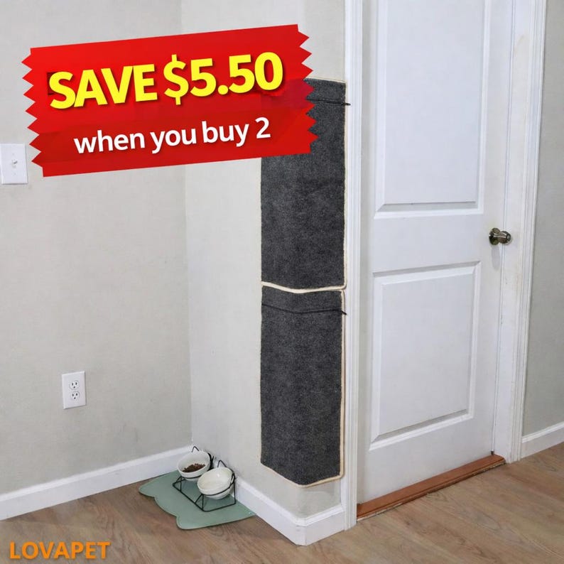 May include: A dark gray cat scratcher attached to a wall next to a white door. The scratcher has a light-colored trim and a pocket. A red banner with the text "SAVE $5.50 when you buy 2" is in the image. A cat bowl set is on the floor.