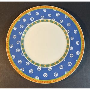 May include: A decorative ceramic plate with a white center and a blue border adorned with white swirl designs. The plate features a green and yellow inner border, and an orange rope-like outer rim. This plate is suitable for serving food.