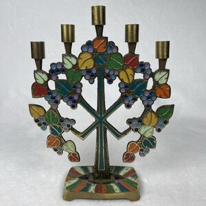 May include: A brass candelabra featuring five candle holders and a central tree-like structure decorated with colorful enamel in shades of red, orange, yellow, green, and blue, depicting clusters of grapes and leaves on a square base.