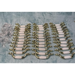 May include: A collection of cabinet handles with a gold finish and white ceramic center. The handles are arranged in neat rows on a light blue surface, with a small pile of screws visible on the left.
