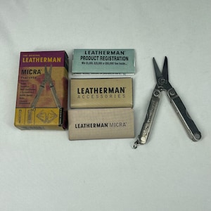 May include: A Leatherman Micra multi-tool with its original packaging, including a box labeled The Original Leatherman Micra, a product registration card, an accessories booklet, and a Leatherman Micra manual, all displayed on a plain surface.