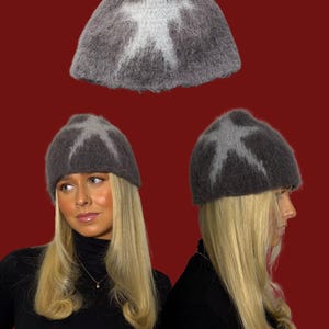 Może przedstawiać: Szara czapka z białym wzorem w kształcie gwiazdy. Czapka, wykonana z puszystego materiału, jest pokazana w kilku widokach na czerwonym tle. Osoba z blond włosami i czarnym golfem ma na sobie czapkę.