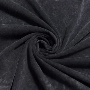May include: Close-up of a dark grey, acid-washed fabric, possibly a t-shirt. The material is soft and has a textured appearance with lighter areas, creating a vintage or distressed look. The fabric is tightly swirled, showing the texture and drape.