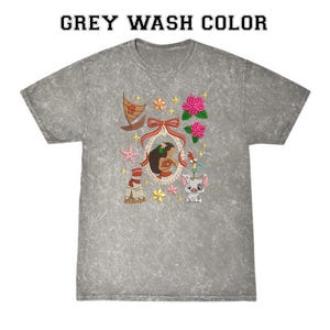 Pode incluir: T-shirt cinza lavado com gola redonda. A camisa apresenta um design bordado colorido com um retrato de uma mulher, um barco, flores e outros personagens de desenhos animados. O texto "GREY WASH COLOR" &eacute; impresso no topo.