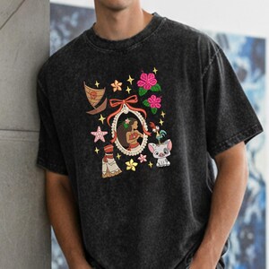 Pode incluir: T-shirt preto com um design bordado colorido. O design inclui um retrato de uma mulher, um barco, flores, estrelas e personagens de desenhos animados. A camisa &eacute; feita de um material macio e confort&aacute;vel.