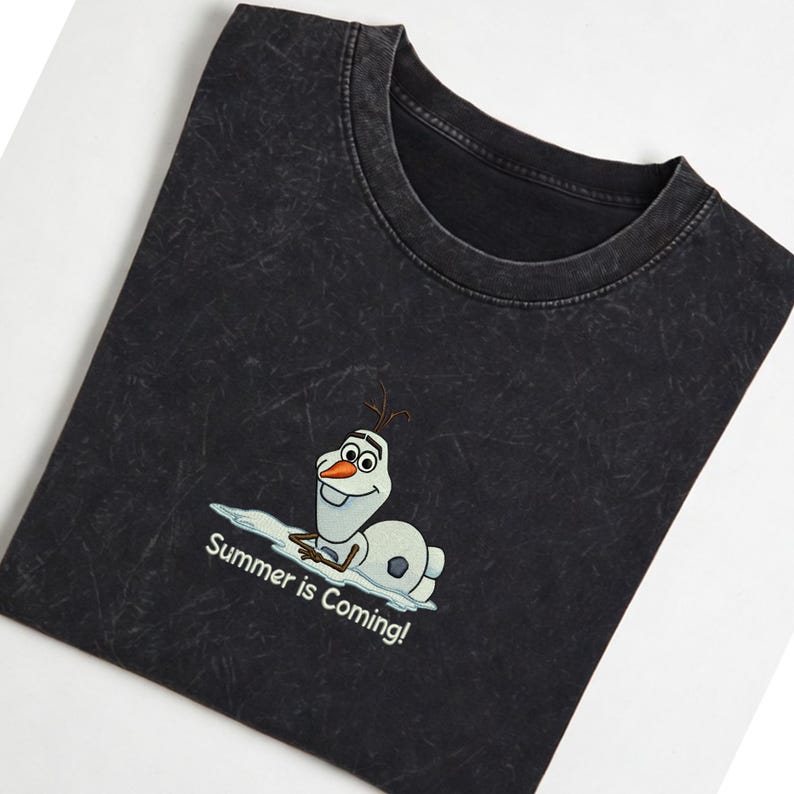 Puede incluir: Camiseta gris oscuro con un dibujo animado de Olaf, tumbado sobre un trozo de nieve. El texto "Summer is Coming!" est&aacute; debajo. La camiseta tiene un lavado vintage.