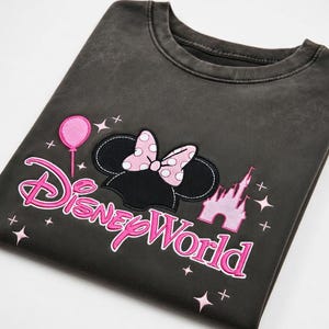 May include: Dark gray sweatshirt featuring a Minnie Mouse design with a polka dot bow, a pink balloon, and the words "Disney World" in pink. The design also includes a pink castle.