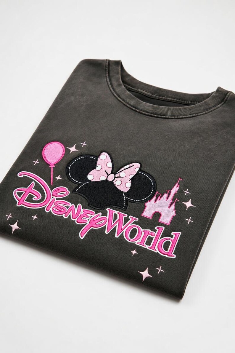 May include: Dark gray sweatshirt featuring a Minnie Mouse design with a polka dot bow, a pink balloon, and the words "Disney World" in pink. The design also includes a pink castle.