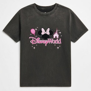 May include: Dark gray t-shirt featuring a pink and black Minnie Mouse design with a bow, balloon, and castle. The words "Disney World" are printed in pink script below the graphic. A casual tee for Disney fans.