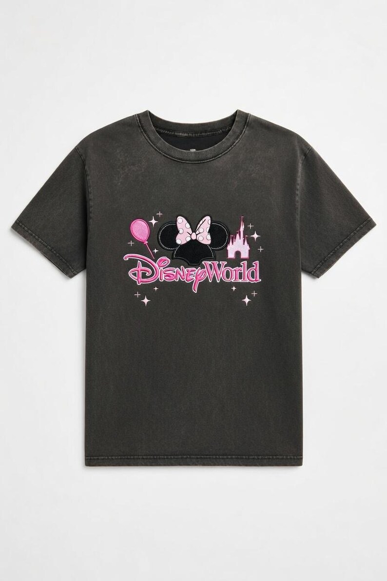 May include: Dark gray t-shirt featuring a pink and black Minnie Mouse design with a bow, balloon, and castle. The words "Disney World" are printed in pink script below the graphic. A casual tee for Disney fans.