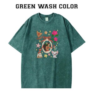 Pode incluir: T-shirt verde lavado com um gr&aacute;fico com uma mulher num quadro, um barco, flores e personagens de desenhos animados. A camisola tem gola redonda e mangas curtas. O texto "GREEN WASH COLOR" est&aacute; impresso no topo.
