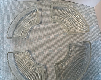 Puede incluir: Cuatro platos de vidrio transparente en forma de abanico con un diseño acanalado. Cada pieza tiene un borde curvo y un borde festoneado. Los platos están dispuestos sobre una superficie a cuadros azul claro y blanco.
