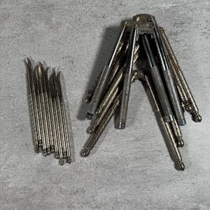 May include: A collection of silver-toned metal seafood picks with textured handles and curved tips, arranged in a row, alongside a cluster of hinged metal nutcrackers featuring similar textured handles and a metallic finish.