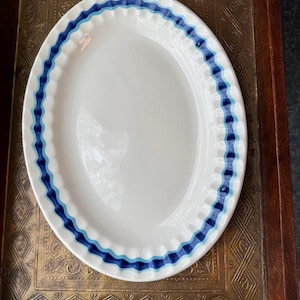 May include: White oval serving platter with a wavy blue and light blue border. The rim has a scalloped edge. The platter is on a decorative brass tray.