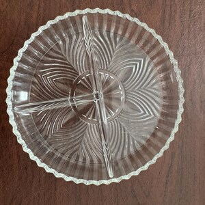Peut inclure: Plat de service en verre transparent à trois compartiments. Le plat a un bord festonné et un motif central rayonnant. Le motif présente des lignes courbes, créant un aspect texturé. Idéal pour servir des collations ou des apéritifs.