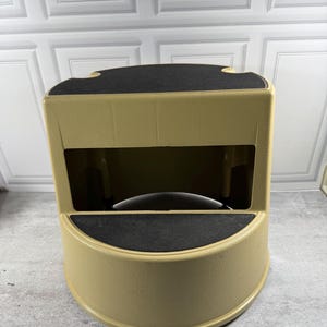 May include: A two-step stool featuring a tan plastic frame with a textured finish. The stool has two wide, curved steps, each topped with a black, non-slip abrasive surface. The design includes a hollow center section between the two steps.