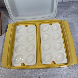 May include: A yellow plastic deviled egg carrier tray with two removable white inserts, each featuring eight oval-shaped indentations for holding eggs. The set includes a large, rectangular, off-white lid that fits over the yellow base tray.