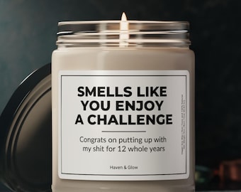 May include: A lit, beige-colored scented candle in a glass jar with a black lid. The label reads "SMELLS LIKE YOU ENJOY A CHALLENGE" and "Congrats on putting up with my shit for 12 whole years." The brand name "Haven & Glow" is also visible.