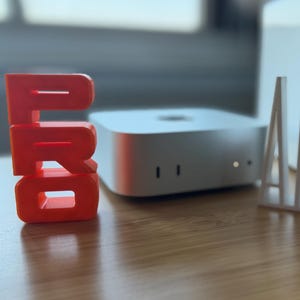 May include: A bright orange "PRO" block is positioned on a wooden surface, alongside a white "AIR" block and a white electronic device. The image conveys a tech or design theme, highlighting typography and product presentation.