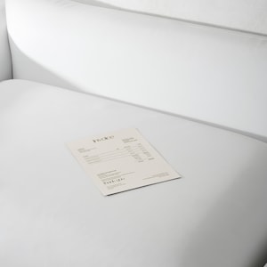May include: A white, minimalist invoice with the word "Invoice" at the top and "Thank You" at the bottom, rests on a white surface. The invoice is printed on a light beige paper, and the background is a plain white.
