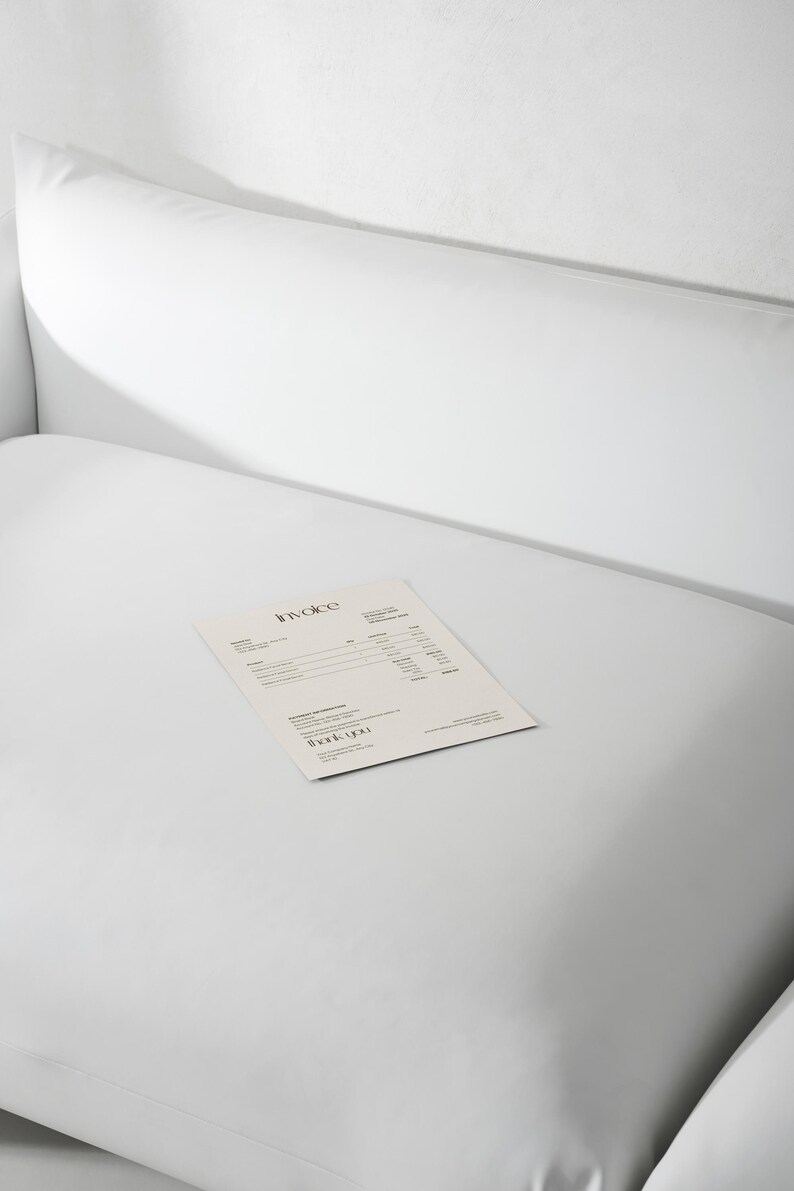 May include: A white, minimalist invoice with the word "Invoice" at the top and "Thank You" at the bottom, rests on a white surface. The invoice is printed on a light beige paper, and the background is a plain white.