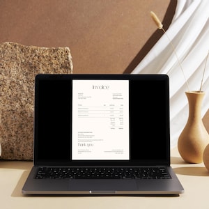 May include: A laptop displays an invoice document with the title "Invoice" in a minimalist design. The laptop is on a light-colored surface, with a textured stone and decorative vases in the background. Dried plants and a white cloth add to the aesthetic.