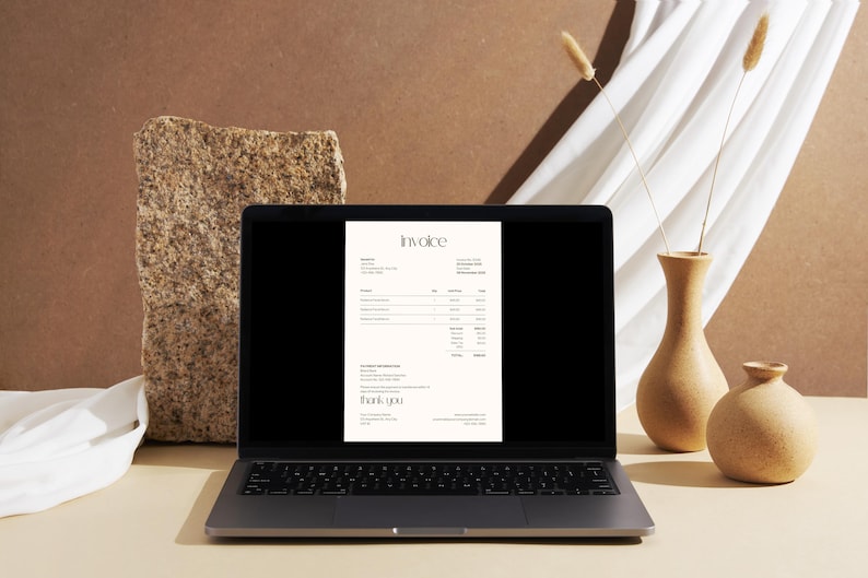 May include: A laptop displays an invoice document with the title "Invoice" in a minimalist design. The laptop is on a light-colored surface, with a textured stone and decorative vases in the background. Dried plants and a white cloth add to the aesthetic.