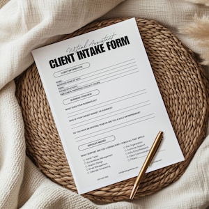 May include: A white Client Intake Form for a Virtual Assistant, with black text and a gold pen. The form includes sections for client information, business overview, and services needed. The form is on a woven mat.