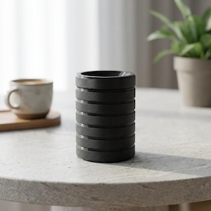 Puede incluir: Un recipiente cilíndrico negro con un diseño texturizado y acanalado. El recipiente está apilado con múltiples secciones, creando una textura visual única. El objeto es probablemente un accesorio de escritorio o un pequeño artículo de almacenamiento.