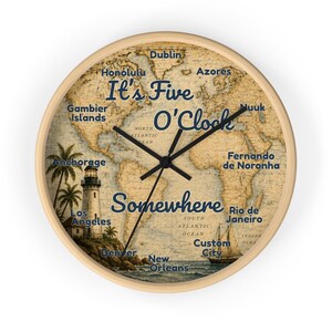 May include: A round wall clock with a light wood frame featuring a vintage world map background. The text It's Five O'Clock Somewhere is printed in blue. The clock face includes illustrations of a lighthouse and a sailboat, along with various city names.