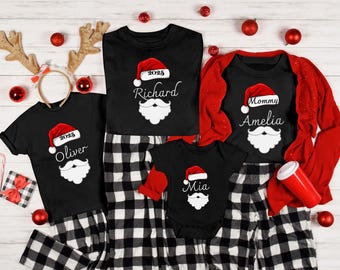May include: Black Christmas family matching pajama sets with Santa hats and names. The shirts have a Santa hat and beard design. The pyjamas are black and white plaid. Red accents include a cardigan, baubles, and a candy cane.