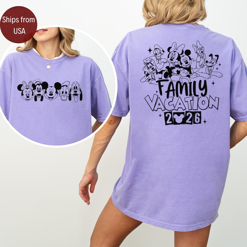 May include: A lilac-colored t-shirt featuring a black graphic of Disney characters on the front and back. The back of the shirt displays the text "FAMILY VACATION 2026" with additional character illustrations. The shirt has a relaxed fit.
