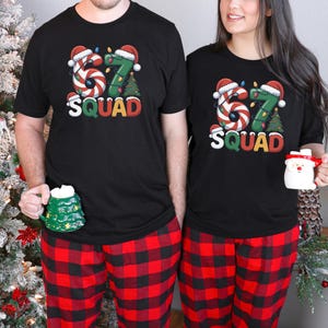 May include: Matching black t-shirts with a festive "67 SQUAD" design, candy cane-style numbers, and Christmas tree graphics. Paired with red and black plaid pajama pants. One person holds a green tree mug, the other a Santa mug.