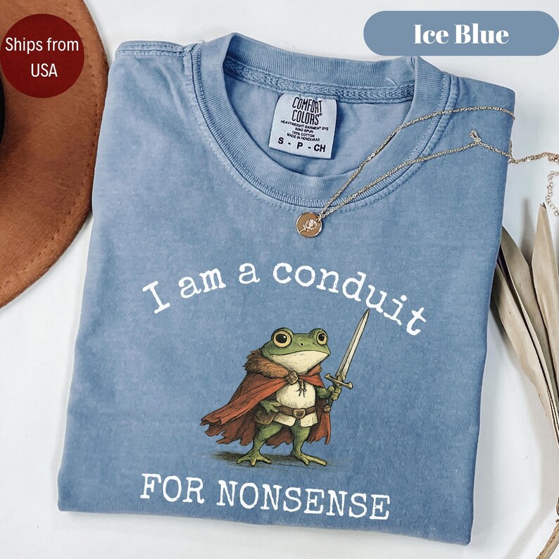 Peut inclure: T-shirt bleu glacier avec l'inscription "I am a conduit FOR NONSENSE" et une grenouille de dessin anim&eacute; portant une cape et une &eacute;p&eacute;e. Un collier dor&eacute; est drap&eacute; sur le t-shirt. Le t-shirt est &eacute;tiquet&eacute; "Comfort Colors" et taille S-CH.