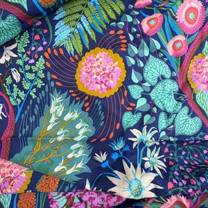 May include: A dark blue fabric featuring a dense, colorful botanical print. The pattern includes bright pink, orange, and white stylized flowers, green fern leaves, and light blue heart-shaped foliage arranged in a complex, layered composition.