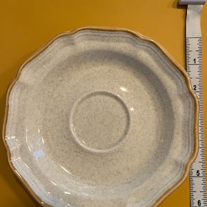 Pu&ograve; includere: Un piattino in ceramica bianco sporco maculato con bordo smerlato e rifinitura marrone. Il piattino ha un diametro di circa 14 cm. Il centro ha un'area incassata per una tazza da t&egrave;.